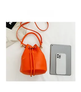 Top view of bright orange drawstring bucket bag next to a tablet for size comparison