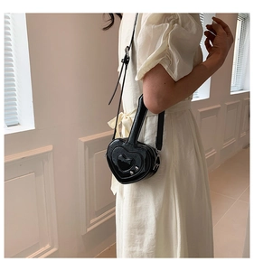 Mini borsa a tracolla nera a forma di cuore indossata da modella in abito bianco