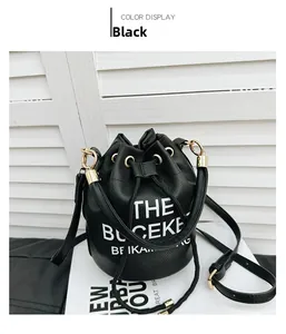 Detail of black drawstring bucket bag with white THE BUCKET text and gold hardware