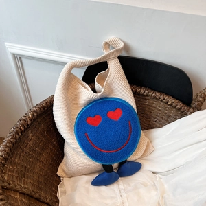 Beige knitted tote bag with blue heart-eyed smiley face and dangling soft legs