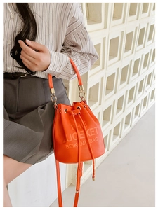 Close-up of vibrant orange drawstring bucket bag with litchi texture and printed text