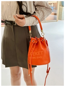Detail of orange drawstring bucket bag showing lychee pattern leather and metal chain strap