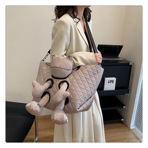 Detail of khaki quilted shoulder bag featuring creative 3D plush doll design and logo