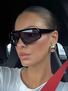 Side view of woman wearing large black wrap-around sunglasses and gold hoop earrings
