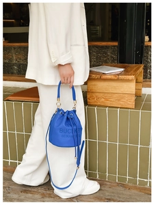 Detail of blue leather drawstring bucket bag with logo and adjustable shoulder strap