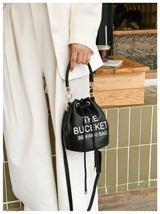 Detail of black drawstring bucket bag featuring white lettering and golden metal accents