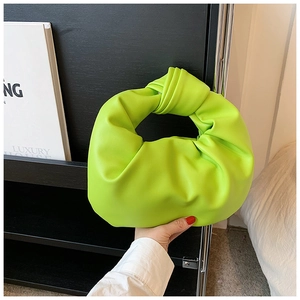 Detail of lime green knotted handle hobo bag with soft pleated texture on a modern shelf