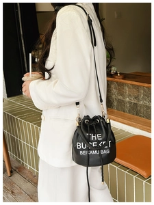 Detail of black leather bucket bag with white typography and gold metal rings