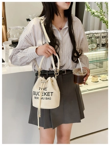 Detail of cream drawstring bucket bag featuring black text and gold hardware accents