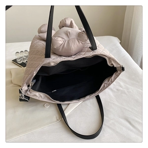 Detail view of beige quilted tote bag featuring a cute plush bear head decoration