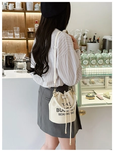 Detail of cream drawstring bucket bag with litchi grain texture and printed text