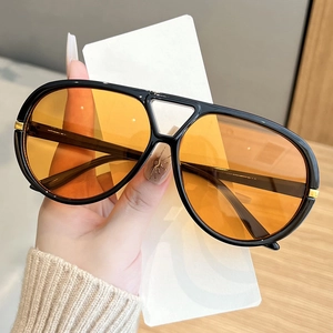 Detail of aviator sunglasses with amber lenses, black frames, and gold metal accents