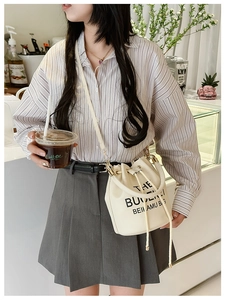 Detail of a beige drawstring bucket bag with black lettering worn by a model in a cafe
