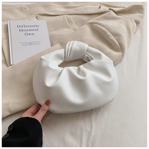 Detail of white pleated cloud bag with a knot handle design on beige fabric background