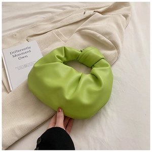 Detail of bright green ruched cloud bag with a unique knotted handle on beige fabric
