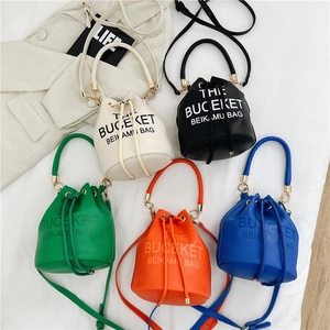 Five assorted colors of drawstring bucket bags with adjustable straps on a white fabric background