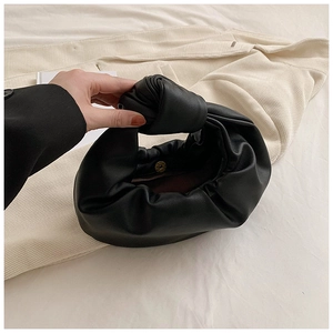 Close-up of black pleated cloud bag featuring knotted handle and gold magnetic closure