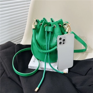 Green drawstring bucket bag in pebble faux leather with gold buckle and shoulder strap