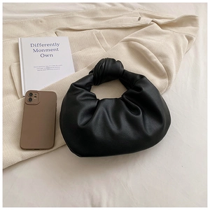 Detail of black pleated croissant bag featuring large knotted handle on soft textured fabric