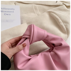 Close-up of pink cloud bag with a knotted handle on a soft neutral fabric background