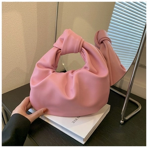 Detail shot of a pink knotted handle bag with pleated leather texture on white books