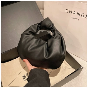 Detail of black pleated knot handbag shown with gift box and white shopping bag