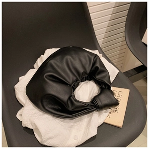 Detail of a black pleated cloud bag with a knotted handle on a white shirt background