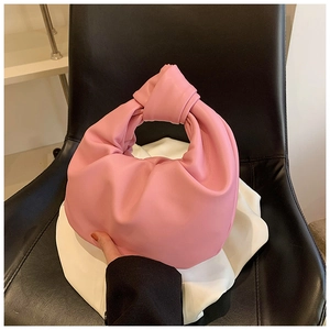 Detail of pink pleated hobo bag with knotted handle on a leather background
