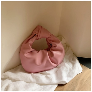 Detail of soft pink pleated cloud bag with knotted handle on a white linen surface