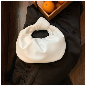 Close-up of white pleated cloud bag with a knotted handle detail on dark clothing background