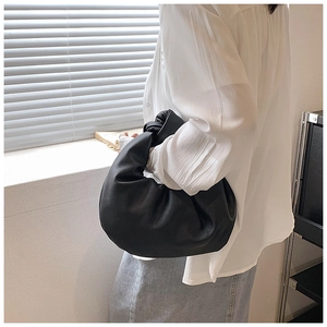 Detail of black pleated cloud bag showing knotted handle and soft synthetic leather texture
