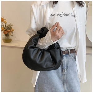 Detail of a black pleated crescent bag with a knotted handle and soft matte PU leather texture