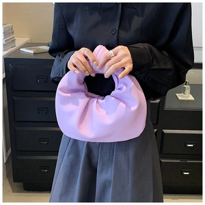Detail of lavender pleated cloud bag with knotted handle held by model in soft lighting