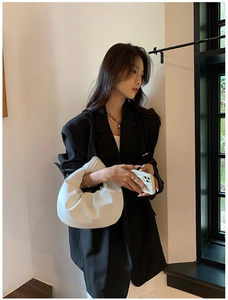 Model holding a minimalist white pleated cloud handbag with knotted handle in a city setting