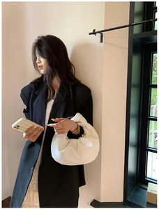 Detail view of white pleated cloud bag held by a model in professional black suit