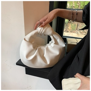 Detail of white pleated cloud bag with a knotted handle shown in an elegant interior