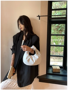 Detailed view of a white ruched cloud bag with a knotted handle held by a stylish model