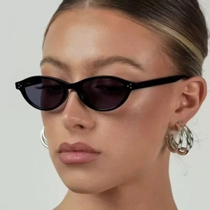 Retro black narrow oval sunglasses and layered silver hoop earrings worn by a model