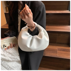 Close-up of a white pleated cloud handbag with knotted handle worn on a woman's wrist