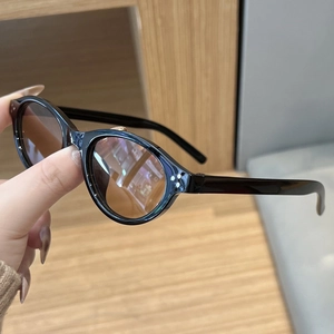 Close-up of black oval sunglasses with brown lenses and triple silver rivet details