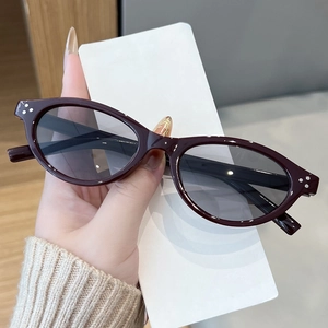 Detailed view of oval dark wine red sunglasses with classic three-dot metal rivets on frame