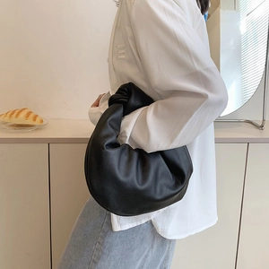 Fashionable black pleated dumpling bag with a knotted handle shown on model's shoulder