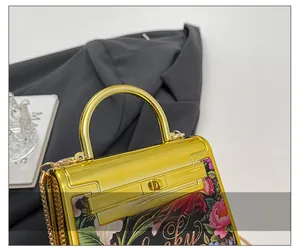 Detail showing the polished golden metal handle and floral print on the acrylic bag