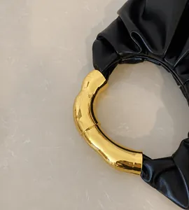 Detailaufnahme der schwarzen Faltenhandtasche mit kreisförmigem goldenem Metallgriff