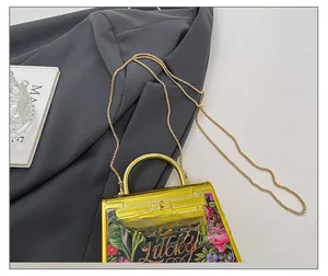 Detail of acrylic floral evening bag with golden metal handle and Lucky typography