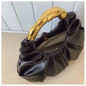 Nahaufnahme einer schwarzen Wolken-Tasche mit goldenem Metallgriff und magnetischem Verschluss