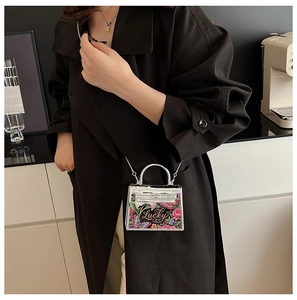 Detail of silver acrylic mini bag with floral print and metallic chain strap worn on coat