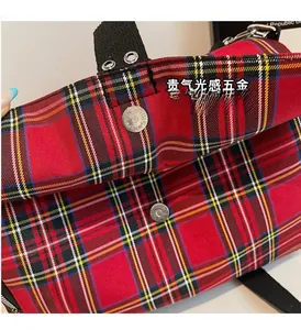 Close-up of the metal magnetic clasp and red tartan plaid fabric on the shoulder bag