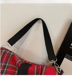 Detail of red plaid canvas bag showing handle stitching and silver metal hook