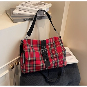 Detail of red tartan canvas shoulder bag featuring leather buckle and metallic zipper